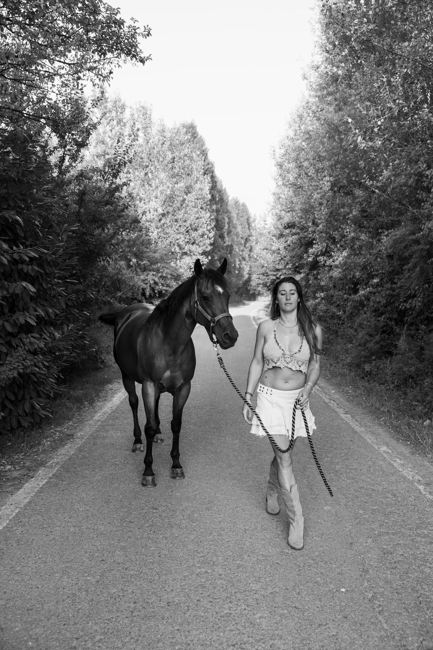 Black and white image of someone leading a horse along a rural path.