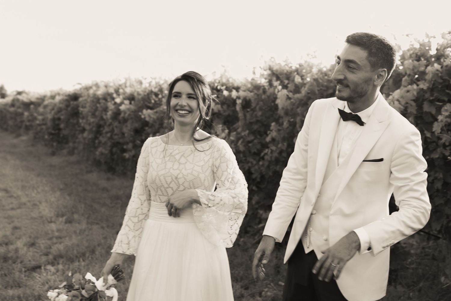A romantic wedding couple walks together outdoors in a black and white photo with a natural background.