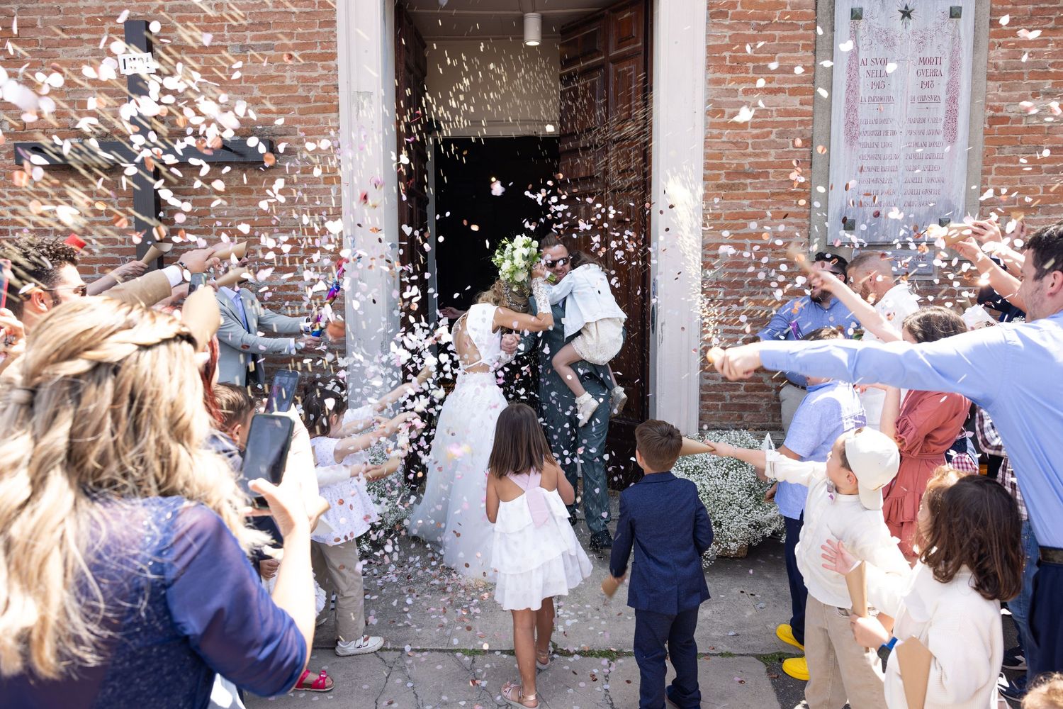 Confetti fills the air as wedding guests celebrate outside a historic brick building.