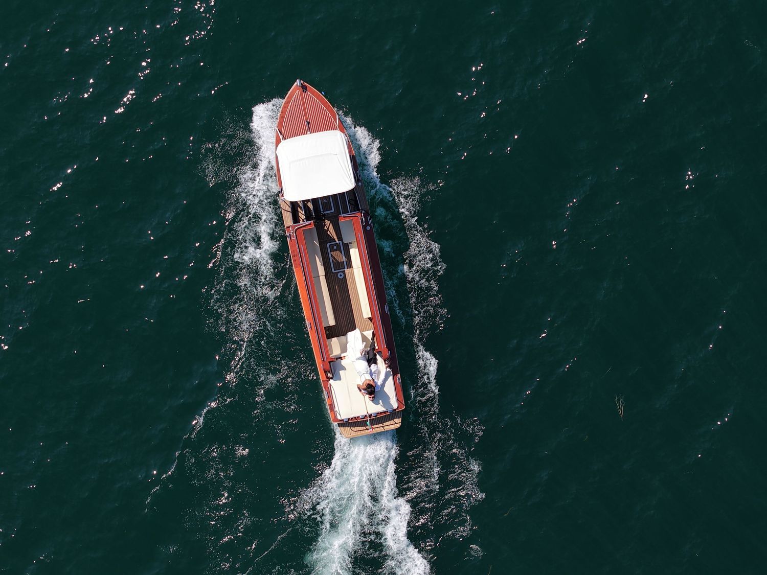 Aerial view of a red and white speedboat cruising through dark turquoise ocean waters creating white wake patterns.