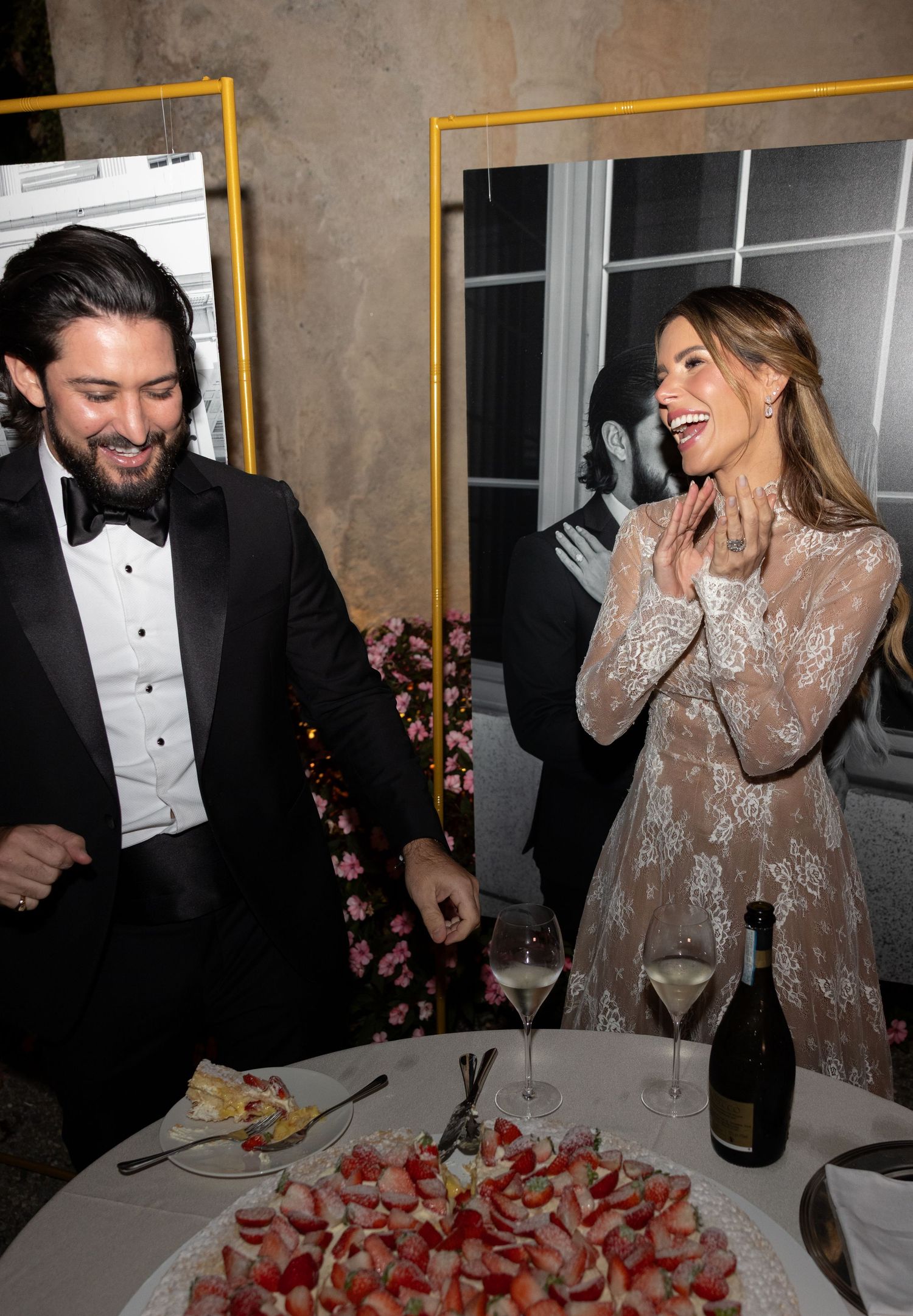A couple in formal attire shares a celebratory moment with champagne and desserts at an elegant party.