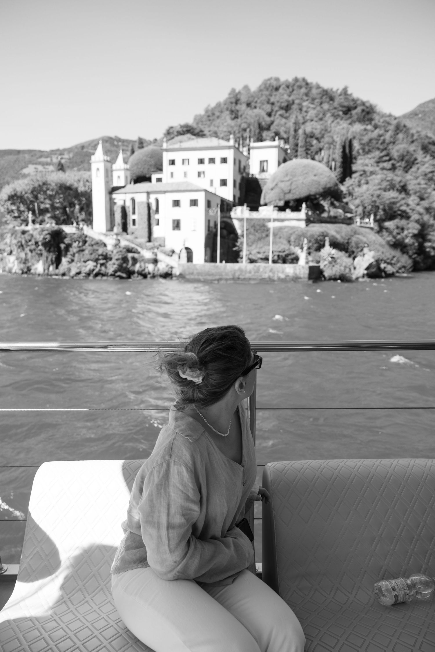 Black and white photo of scenic lakeside boat journey with coastal villas in view.