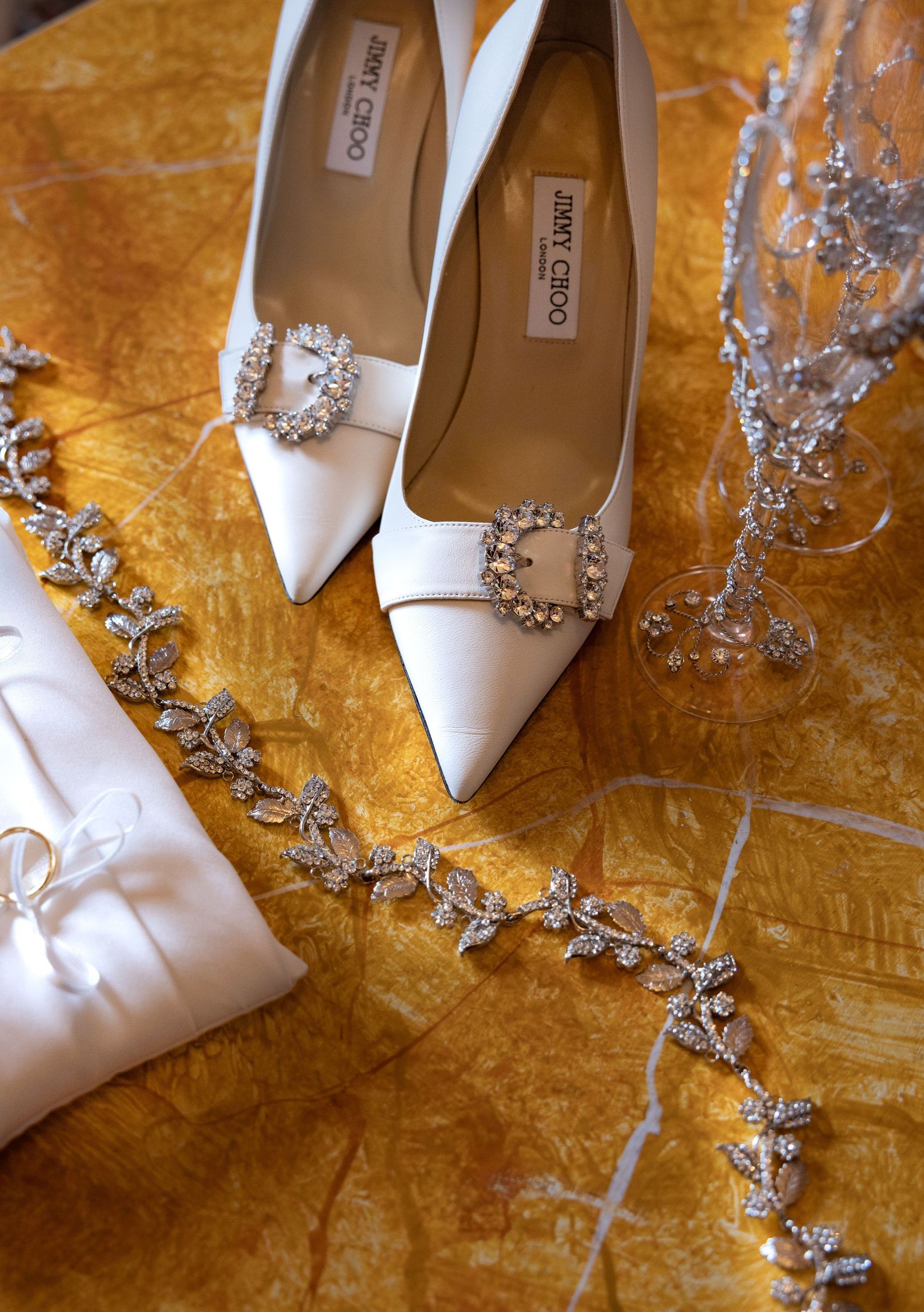 White bridal shoes with crystal embellishments displayed on golden fabric.