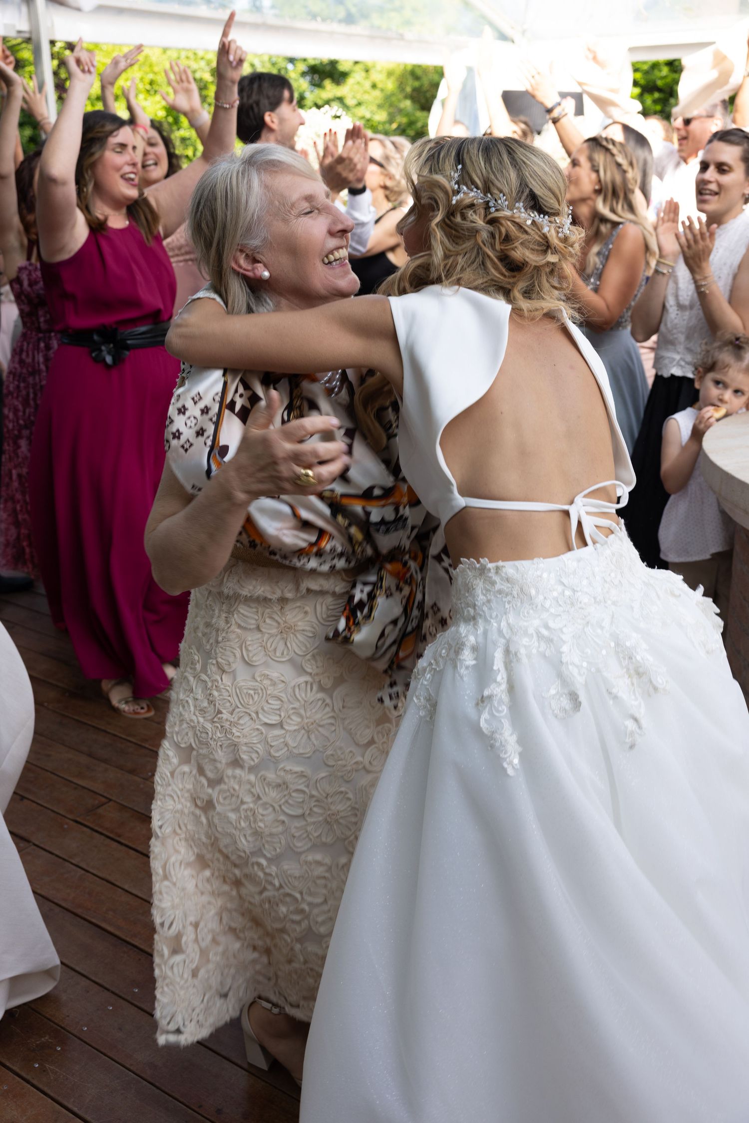 Wedding guests dance and celebrate on a wooden deck during a festive reception.