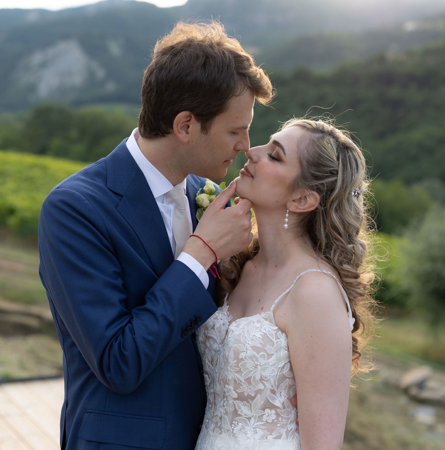 Newlyweds share tender kisses with mountain vineyard landscape in background.