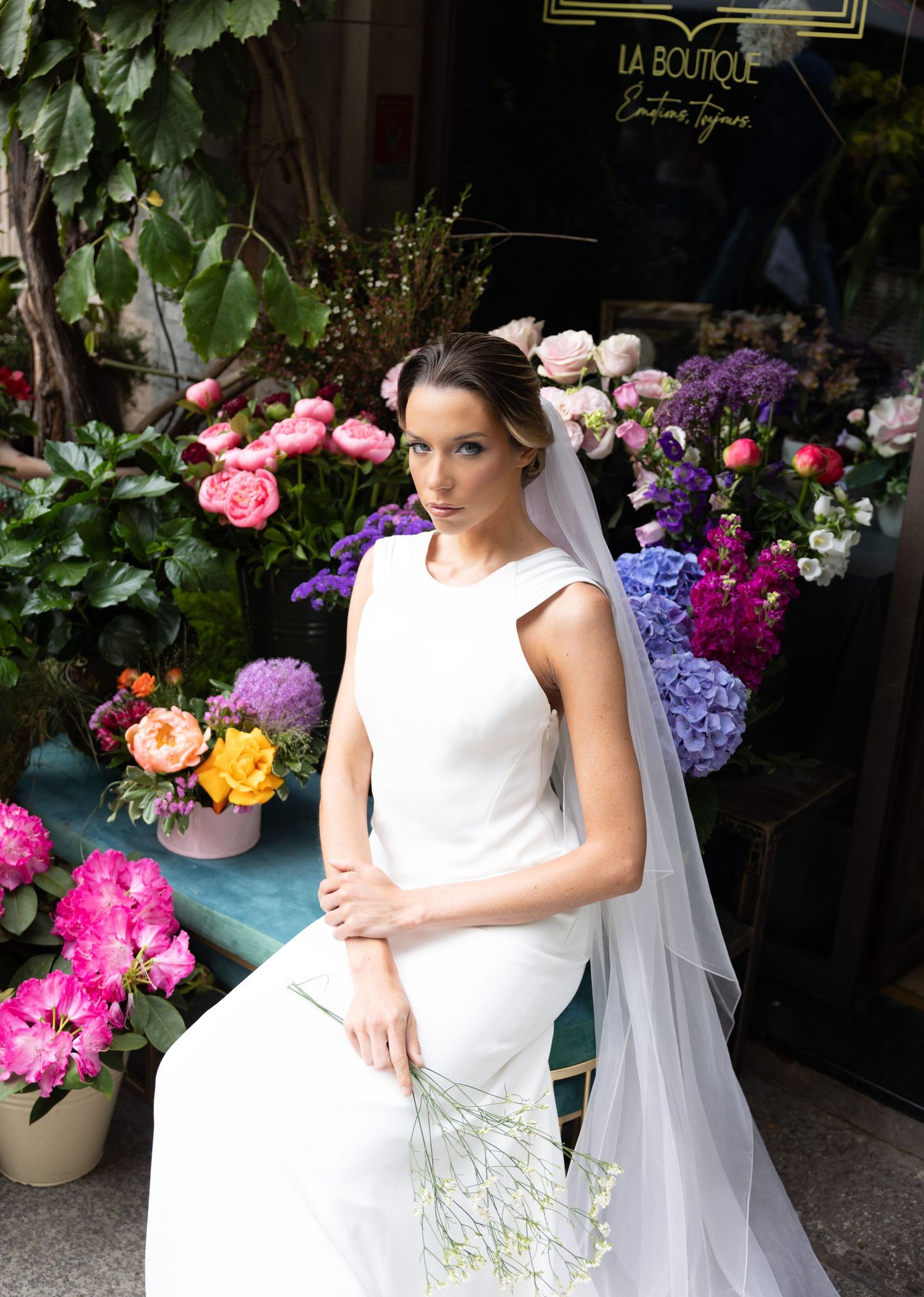 Elegant bridal portrait with flowing veil against a backdrop of colorful flowers and greenery.