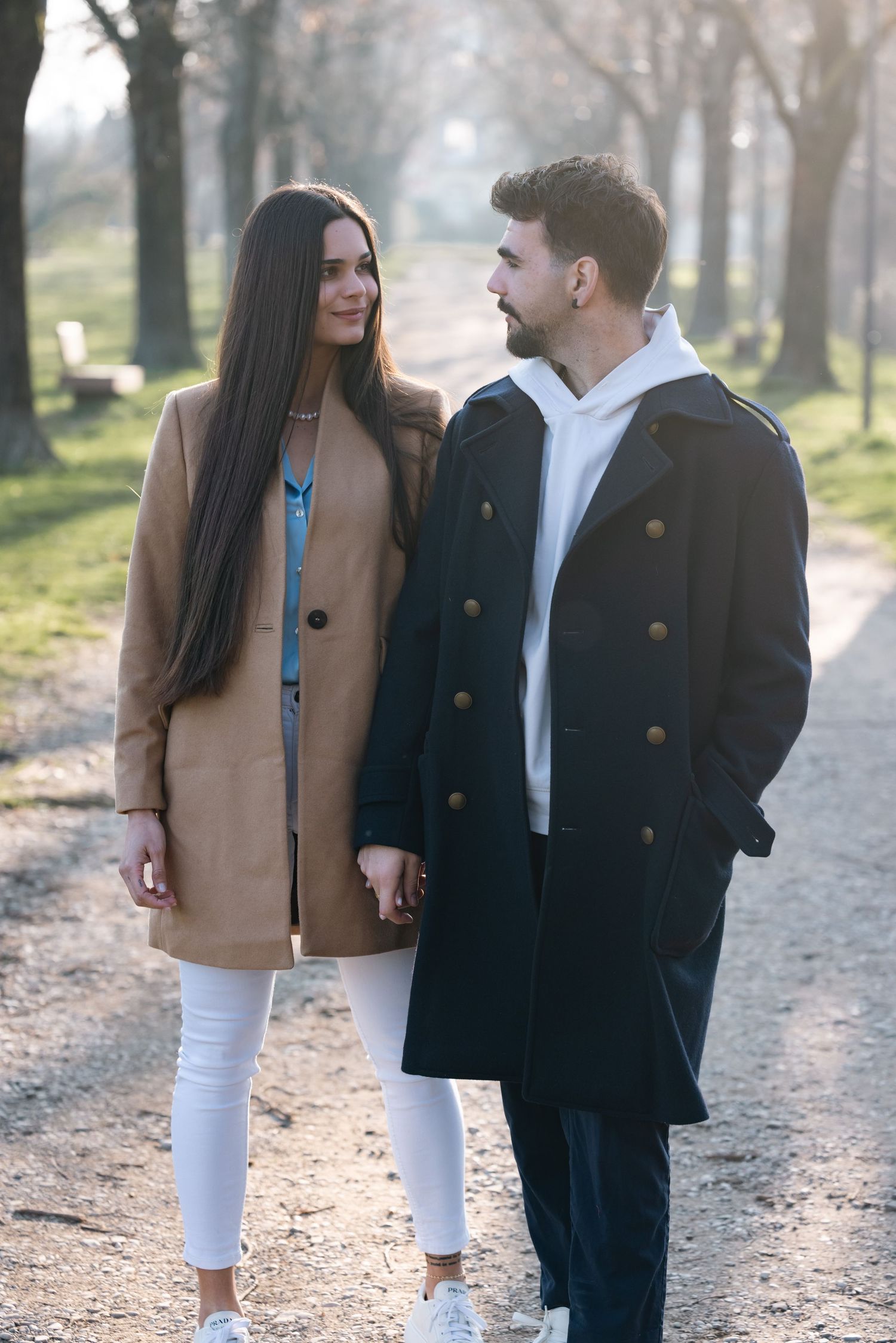 Couple strolling down a park path in winter coats during golden hour.