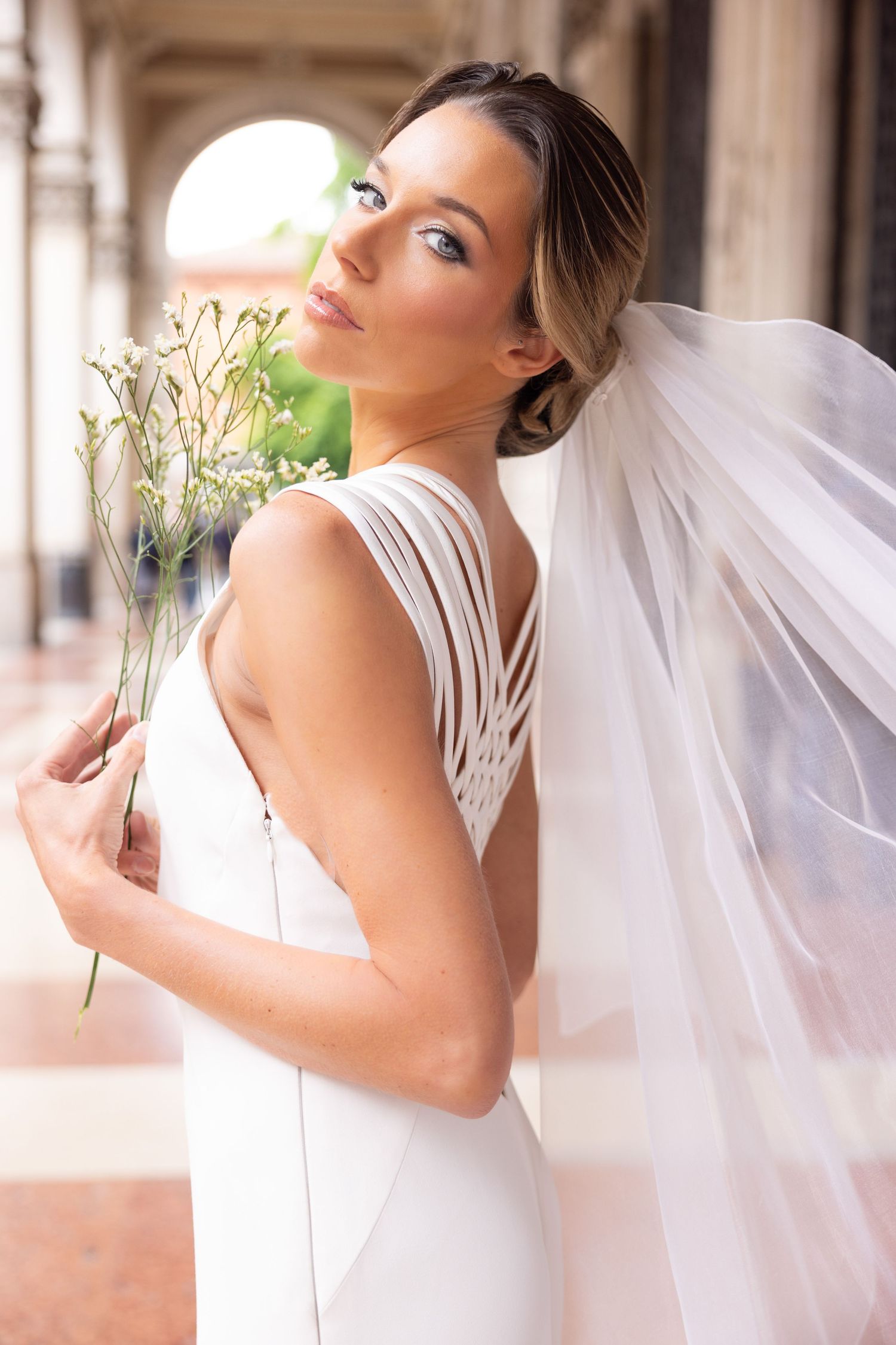 White bridal gown with flowing veil photographed in dramatic poses against classical architecture.