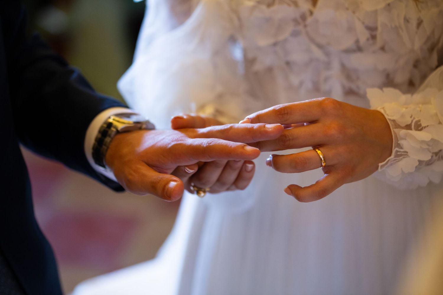 Close-up details of hands and white lace from a wedding dress.