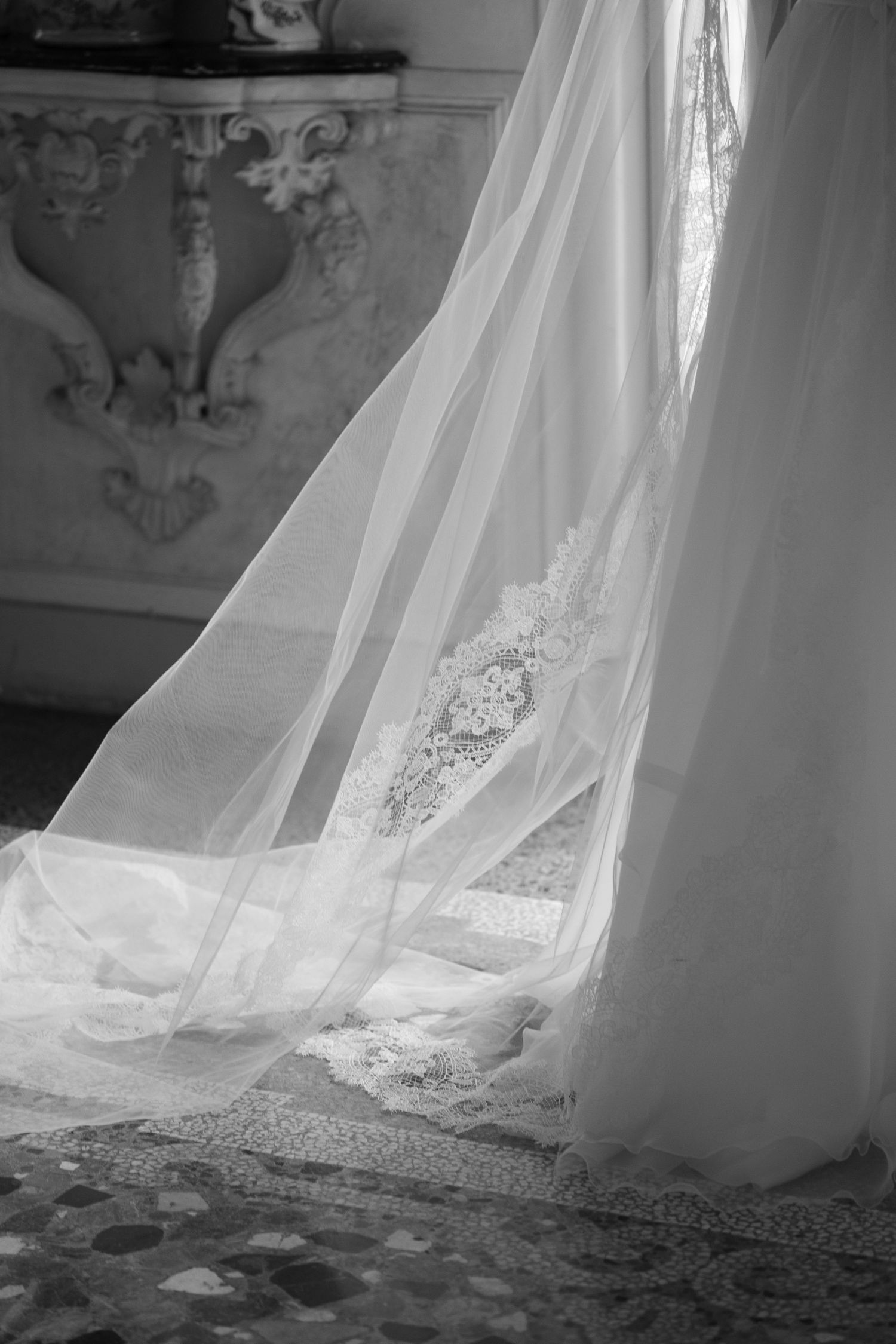 Elegant white wedding dress train with intricate lace details photographed in black and white.