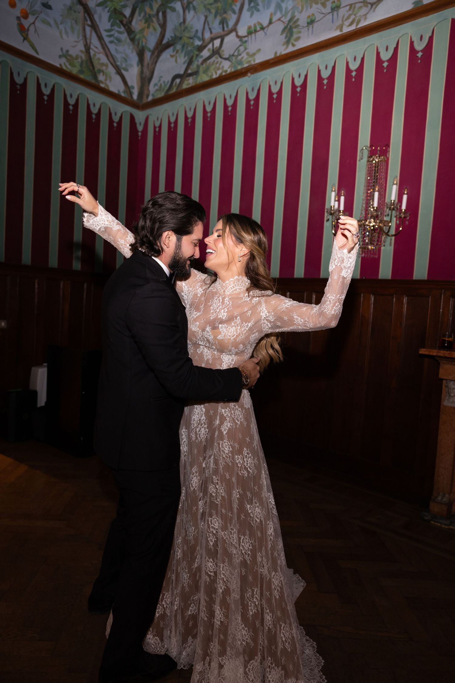 A couple dances together at an elegant venue with red and white striped walls in the background.