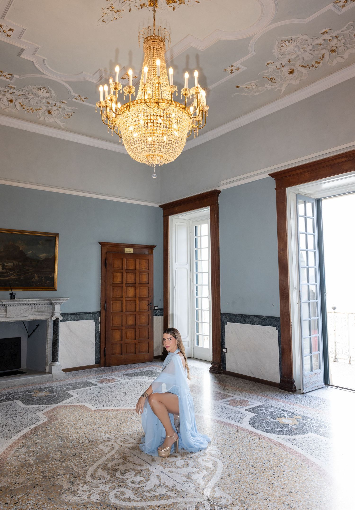 Elegant room with ornate crystal chandelier, decorative ceiling moldings, and patterned marble floors in a historic building.