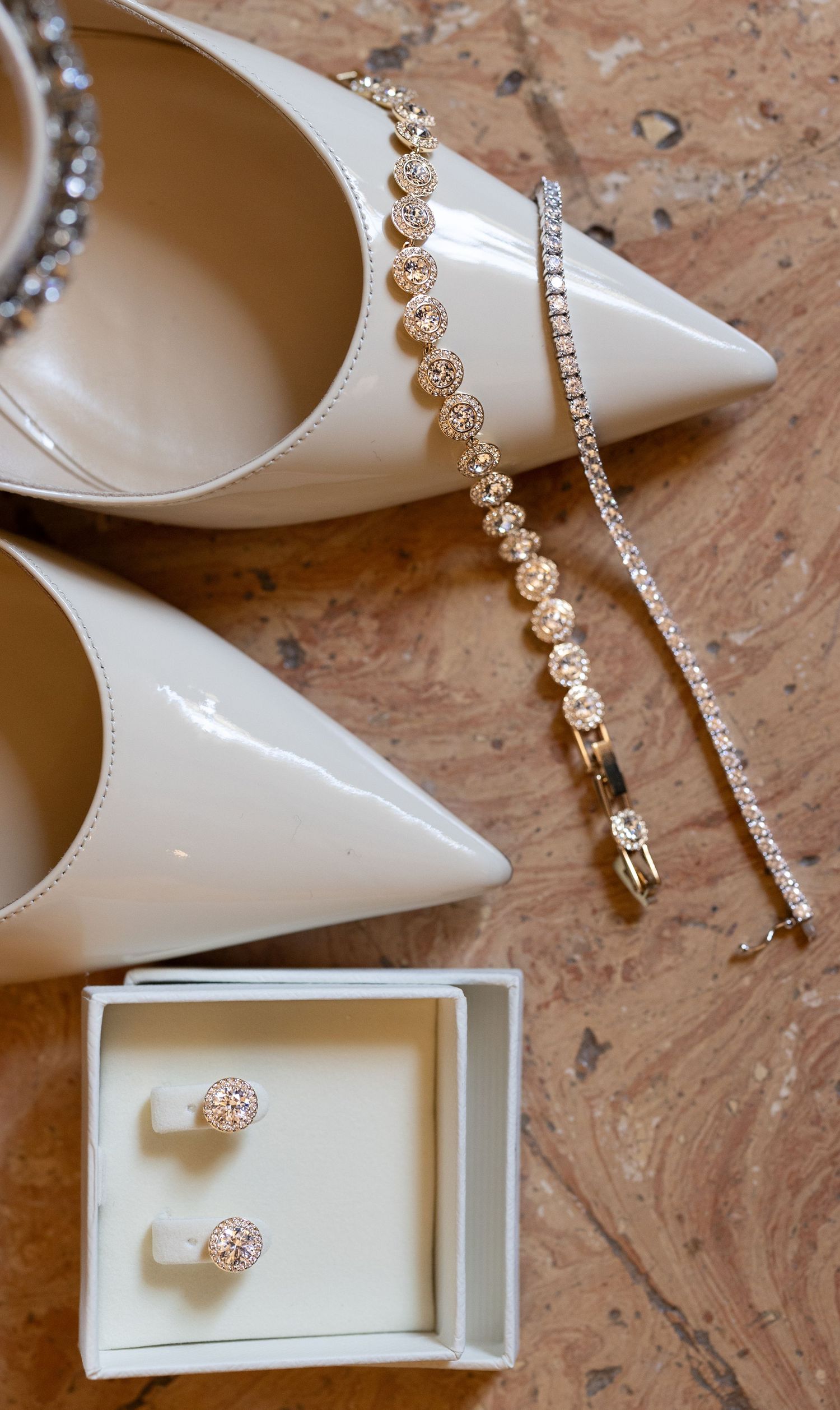 Elegant white bridal shoes with crystal jewelry and diamond accessories on marble surface.