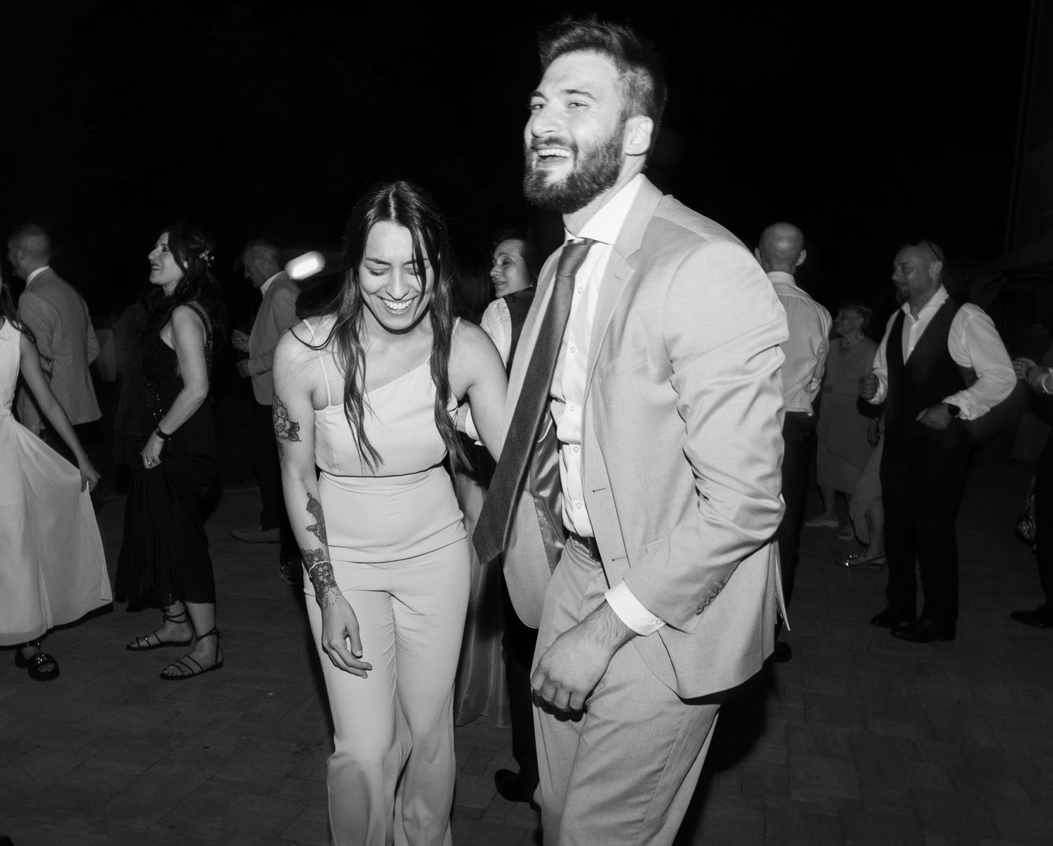 Black and white photo of wedding guests dancing at a nighttime celebration.