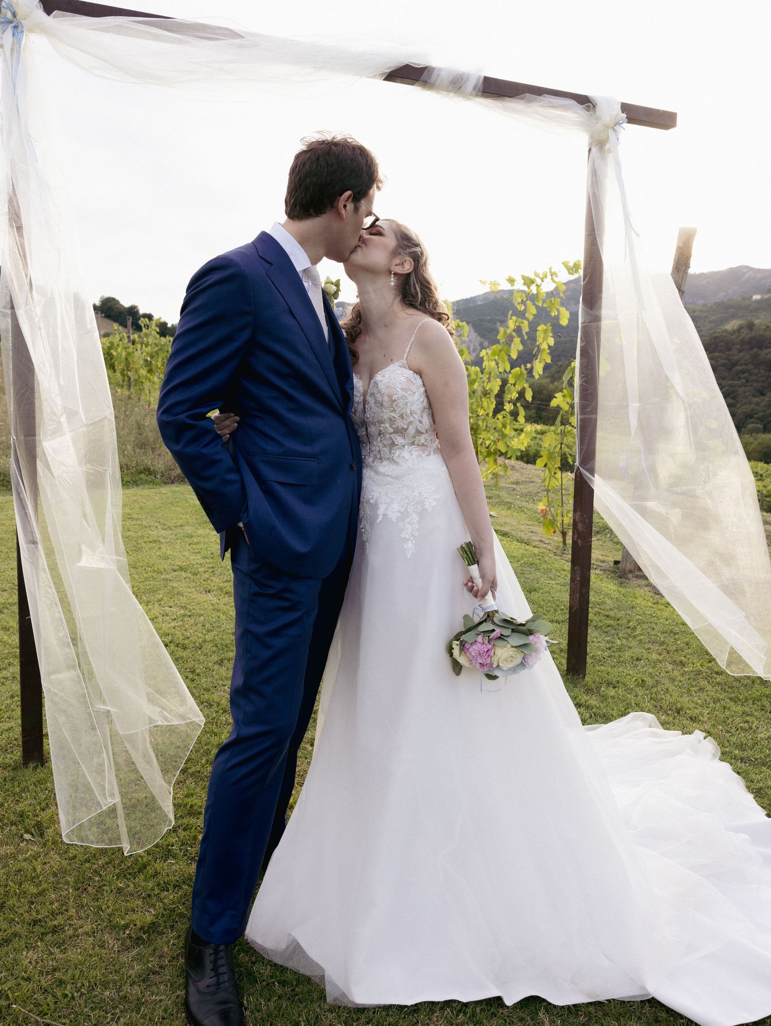 A romantic moment between newlyweds surrounded by flowing white fabric outdoors.