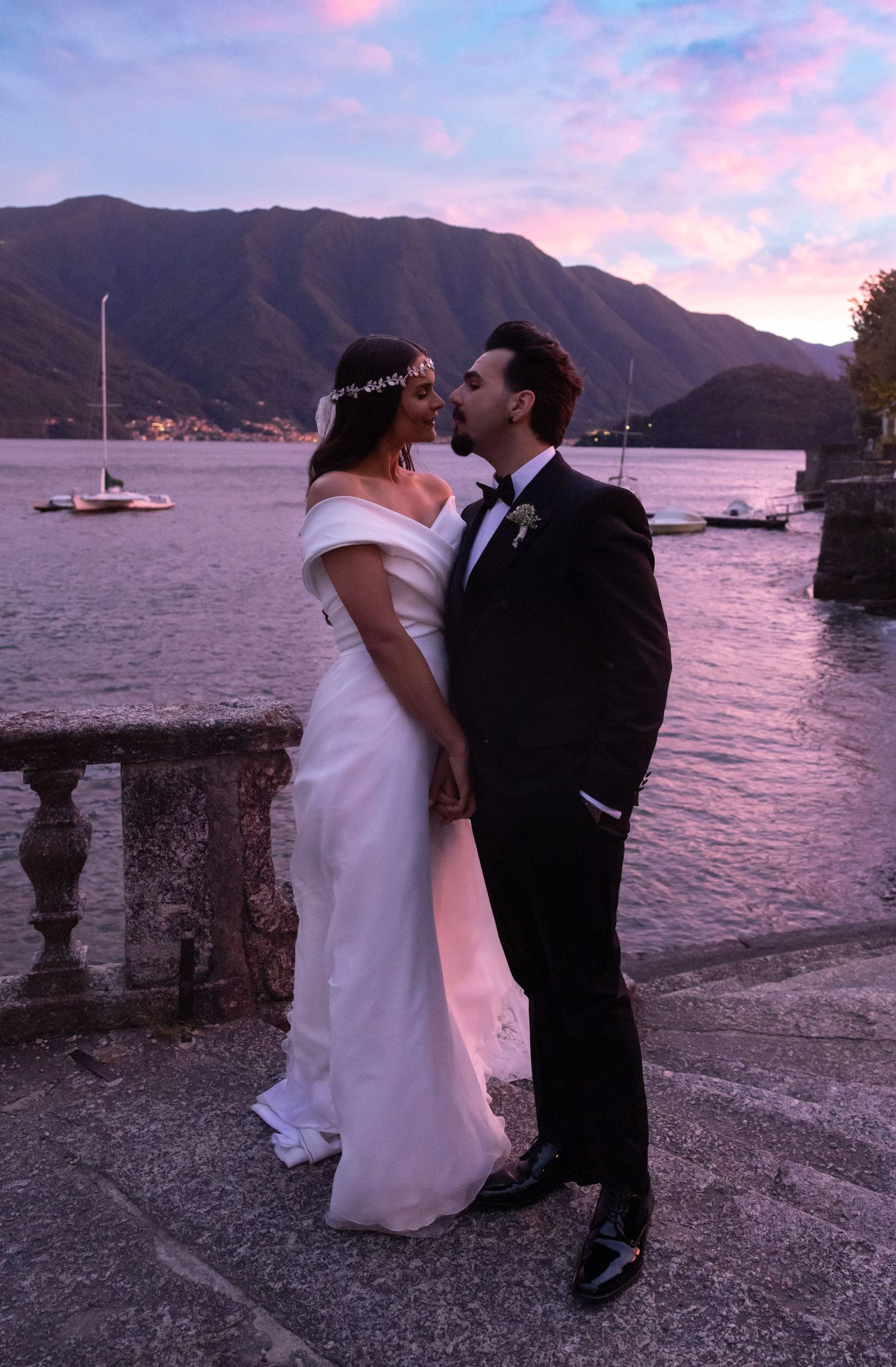 A romantic sunset moment by a lakeside stone wall with mountains in the background.