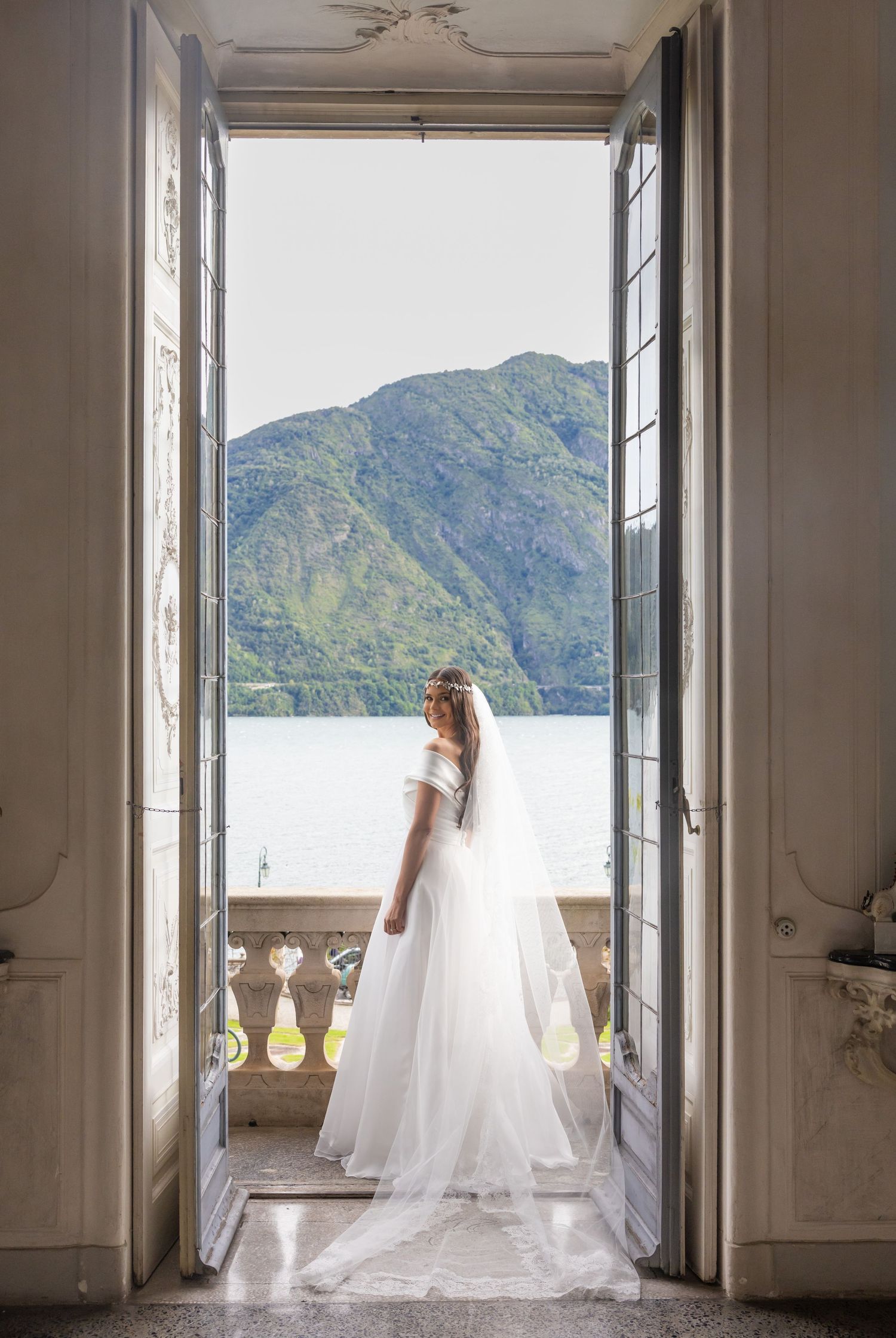 Flowing wedding gown photographed in doorway with scenic mountain lake backdrop.
