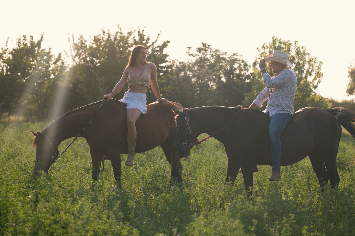 Group walking with horses through a lush green field during golden hour.