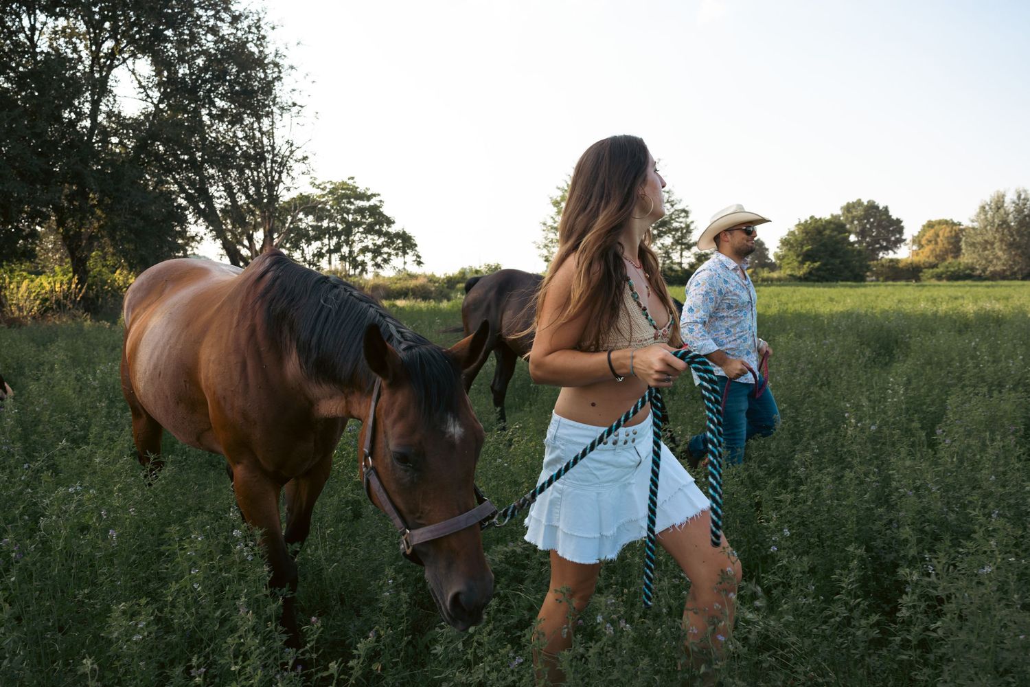Couple on horseback riding through a scenic countryside field at sunset.