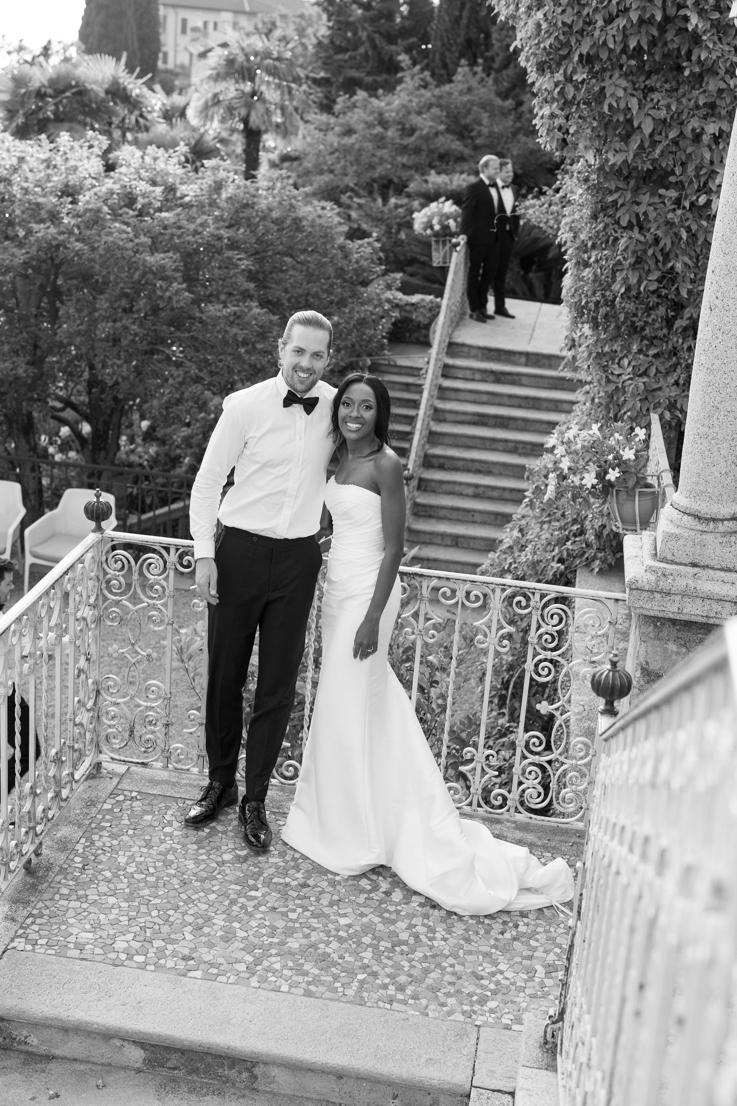 A series of black and white wedding photos showing couples posing by ornate railings and stone steps in a garden setting.