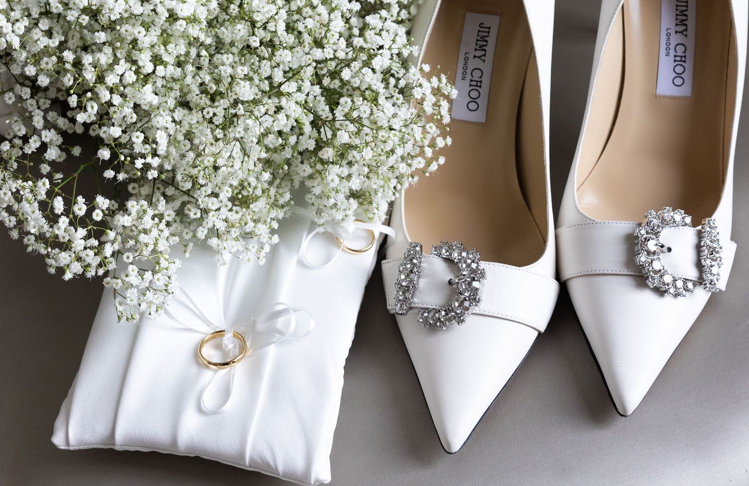 White bridal shoes and baby's breath flowers arranged with a ring pillow.