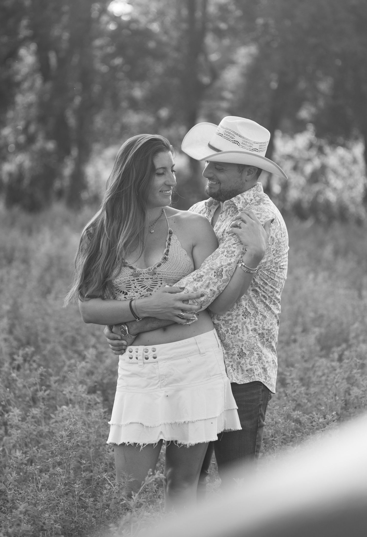 Romantic couple embracing in a meadow wearing casual summer outfits.
