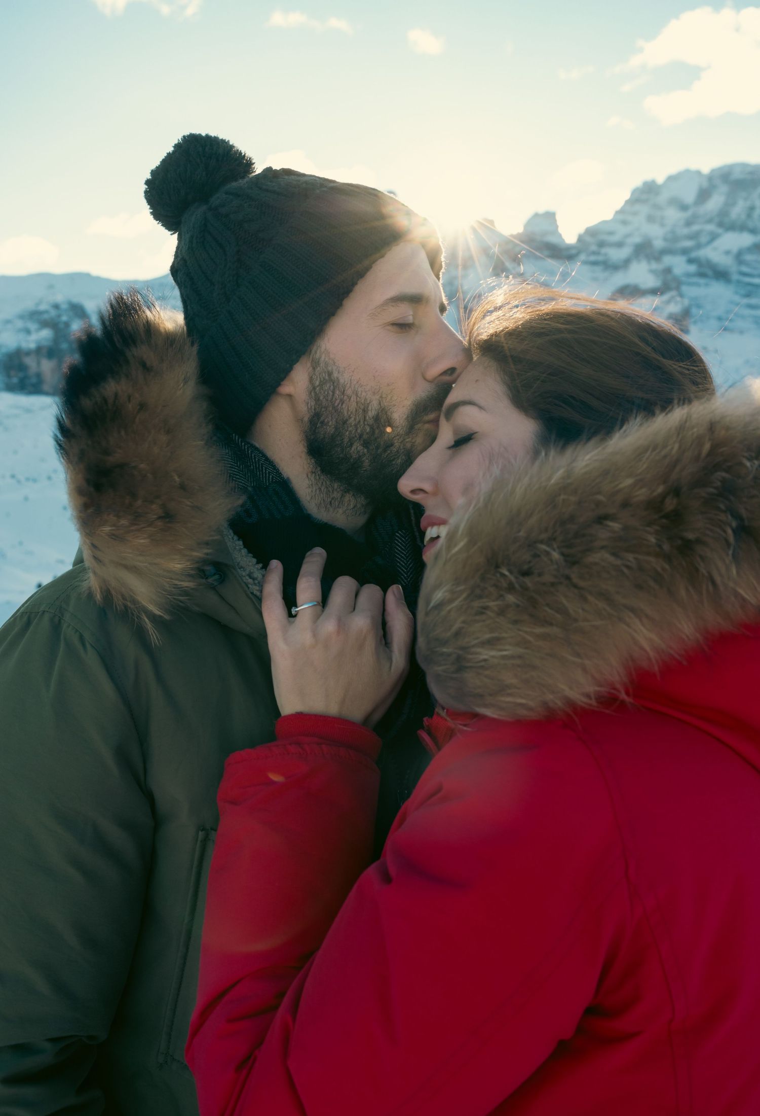 Winter romance scene with couple in warm clothing against snowy mountain backdrop.