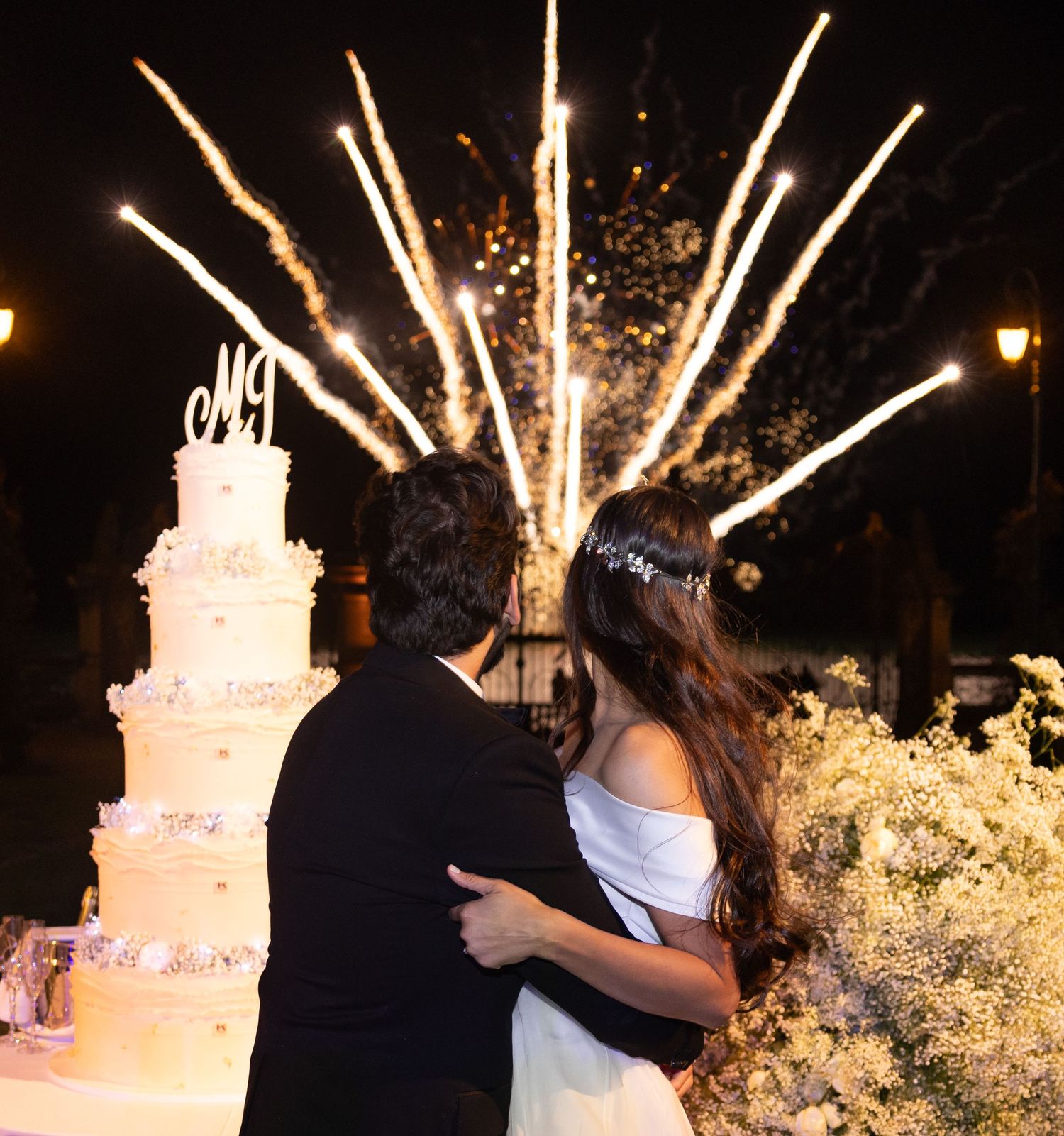 Elegant wedding celebration with sparklers and a white tiered cake at night.