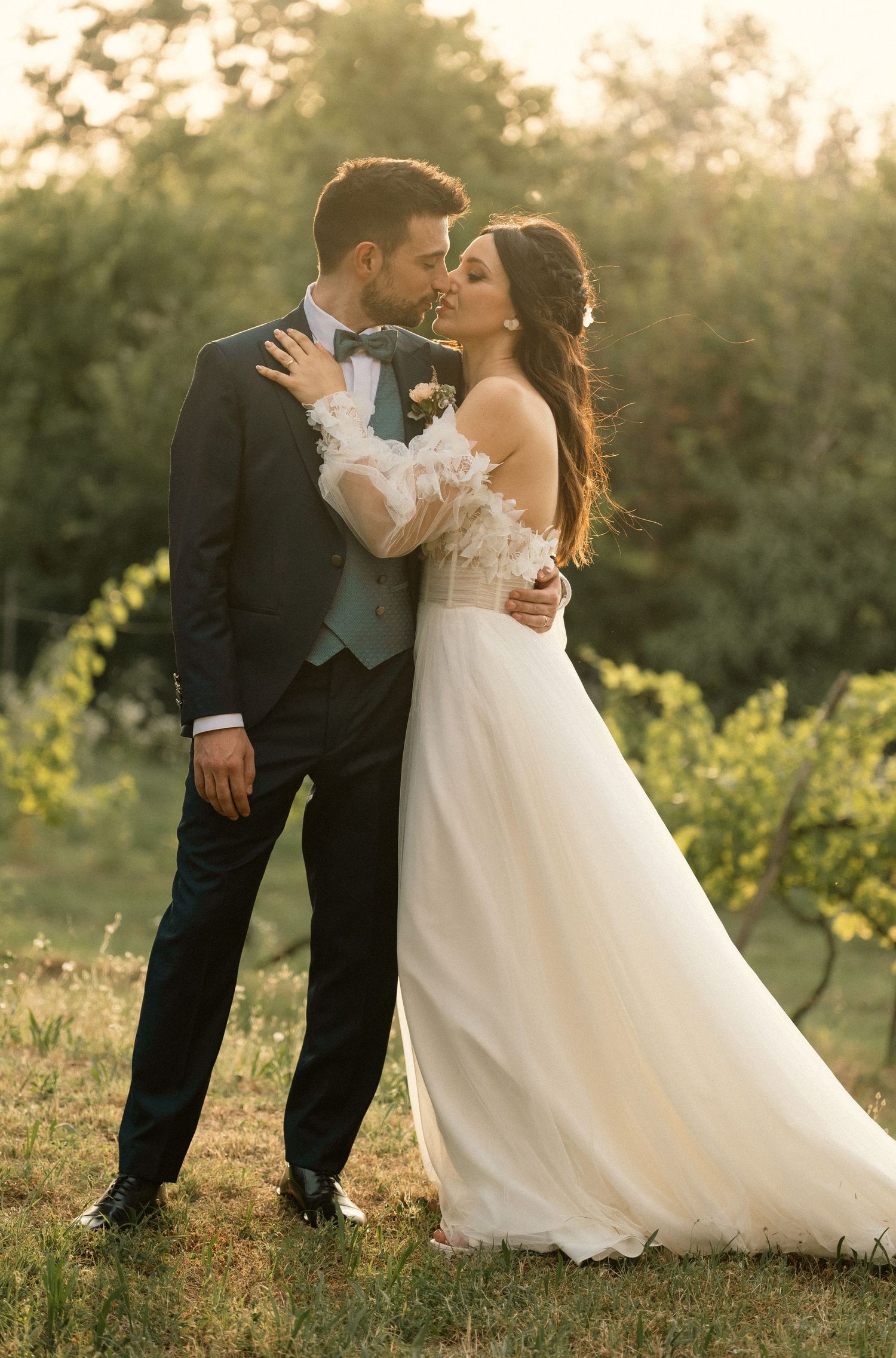 A sunset wedding portrait of a couple in formal attire embracing in a garden setting.
