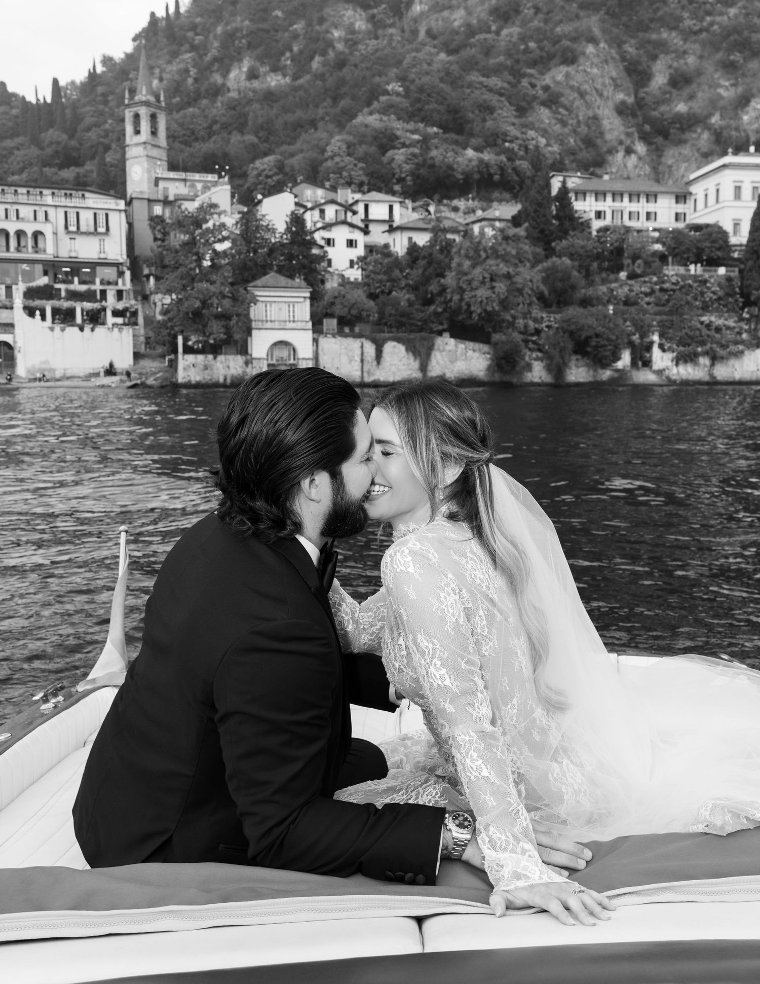 A romantic couple shares tender moments on a boat with Lake Como's scenic shoreline and villas in the background.