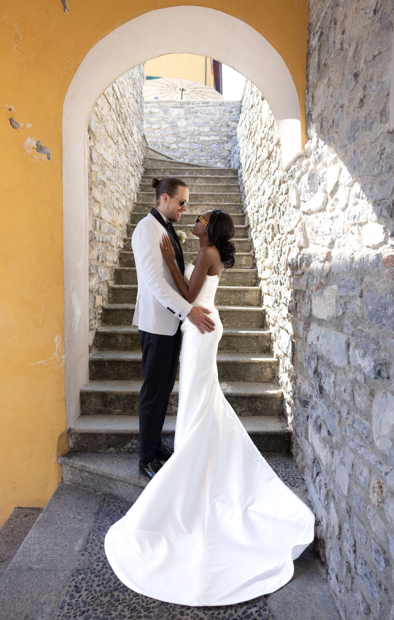 Wedding couple dances and embraces in a series of romantic poses against a rustic stone staircase and yellow wall.