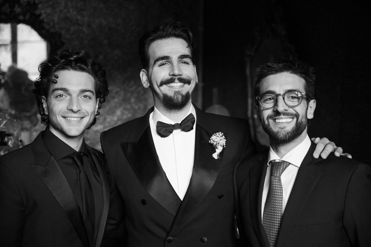Group of groomsmen in formal attire smiling and posing together in black and white.