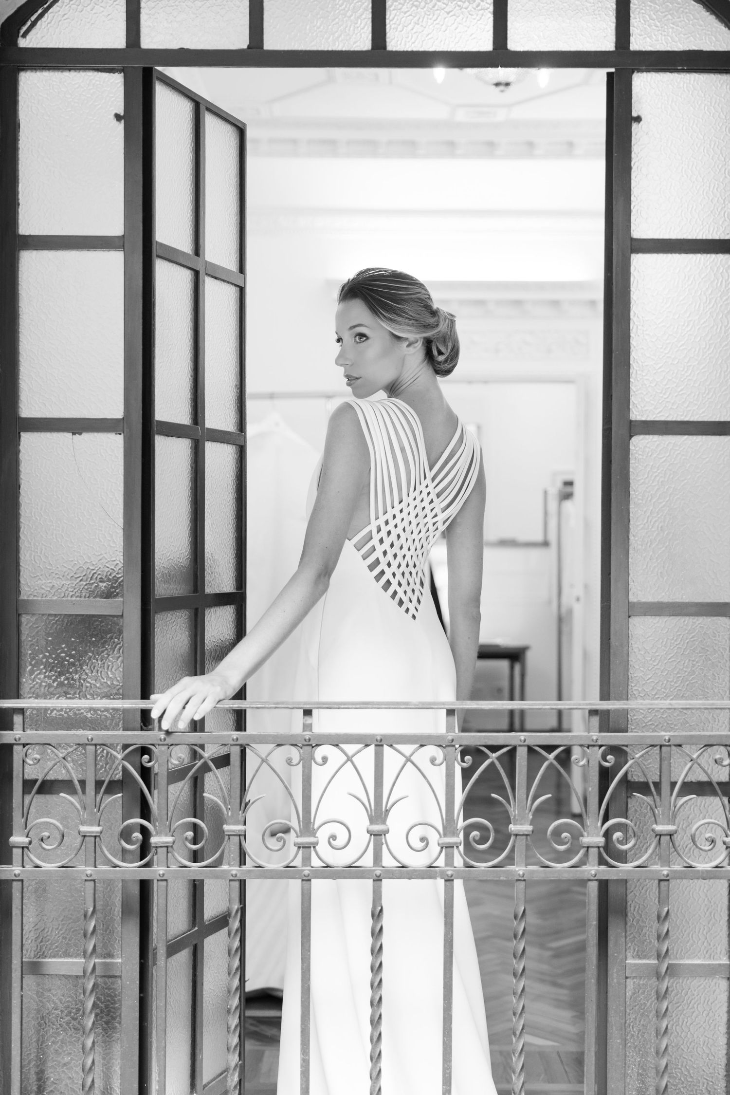 Elegant white dress photographed against ornate metal railing in bright interior hallway.