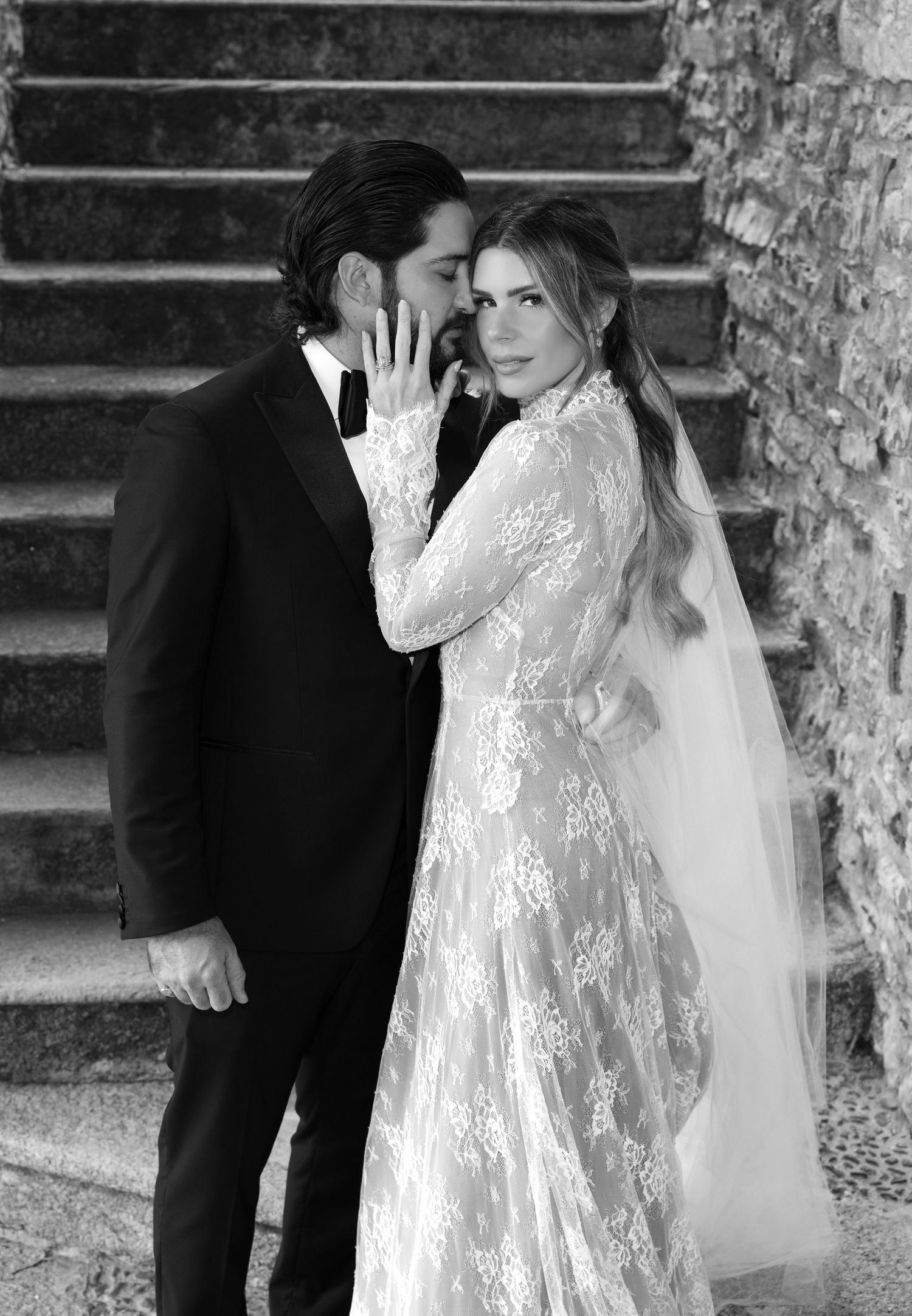 A romantic black and white wedding photo showing a couple in formal attire on stone steps, with the bride wearing lace.