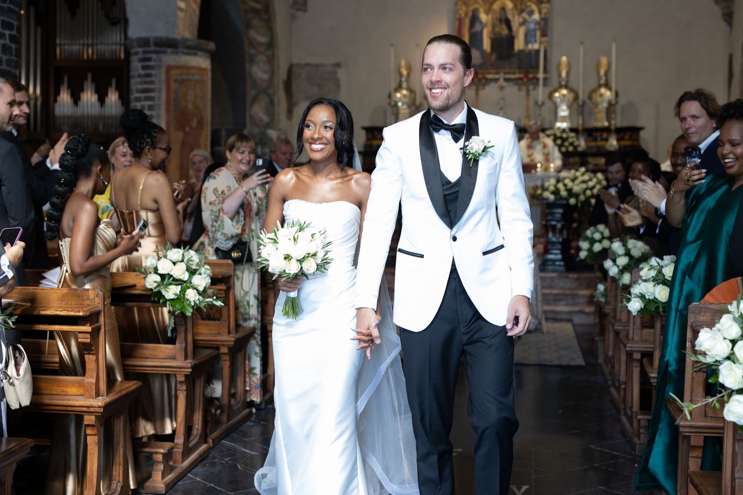 A joyful wedding ceremony moment with guests applauding and floral decorations adorning the church interior.