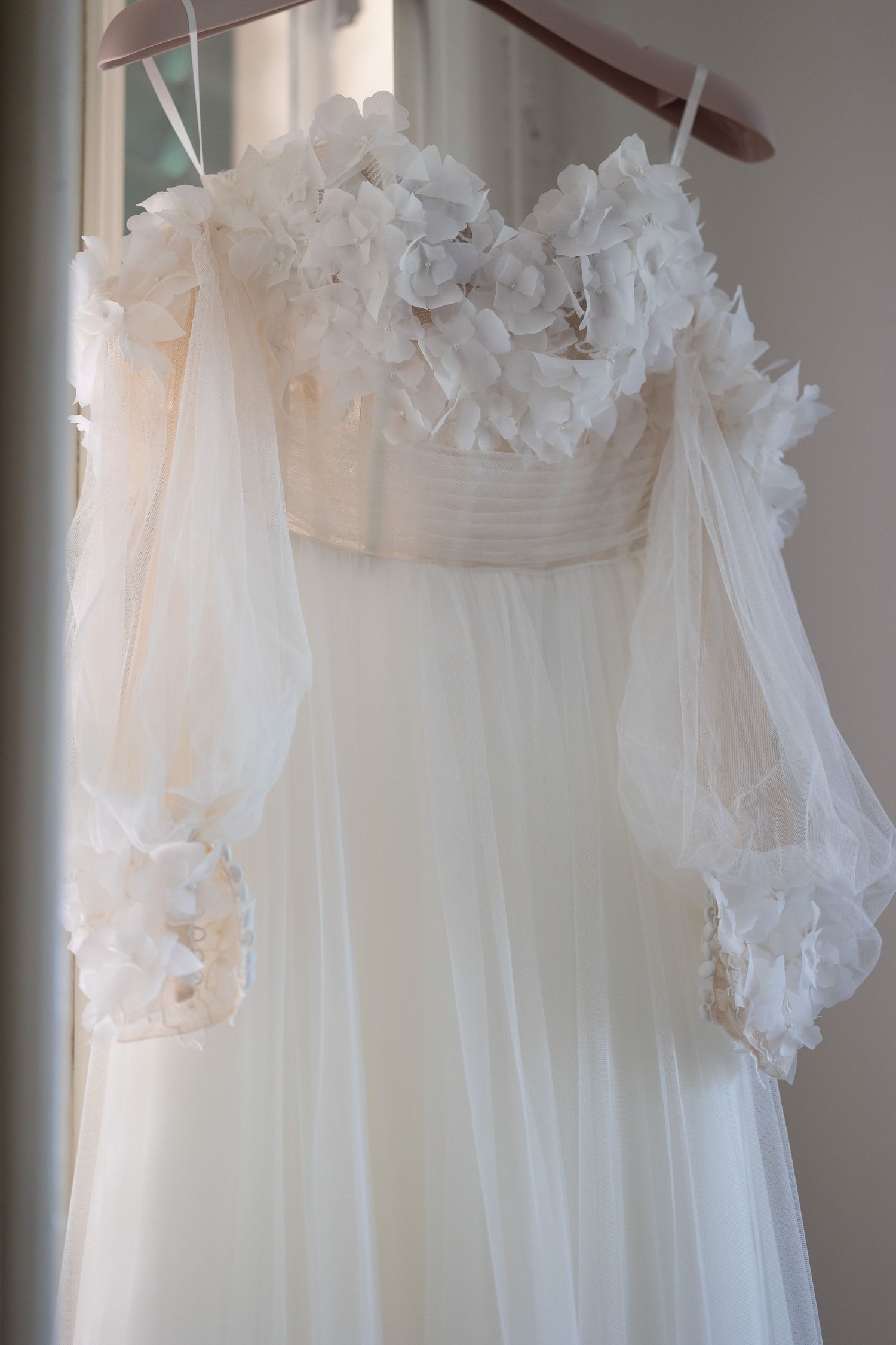 Elegant white wedding dress with delicate floral details and flowing tulle fabric hanging on display.
