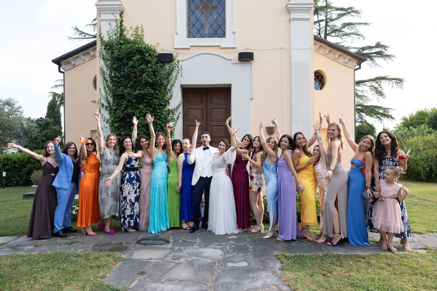 Wedding party group photo in colorful dresses lined up outside a historic stone building.