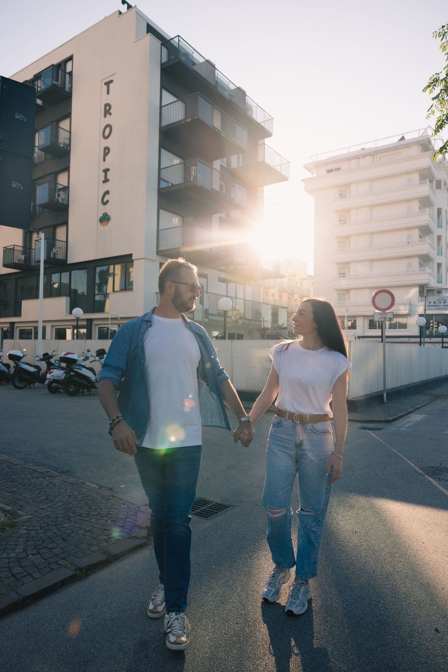 Couple holding hands while walking at sunset in an urban setting.