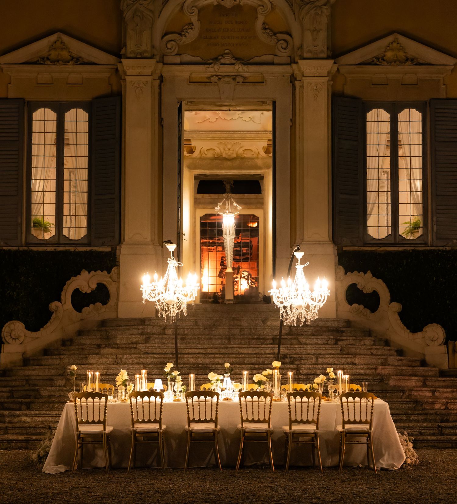 Elegant outdoor dining setup with crystal chandeliers and white tablecloths illuminated at night.