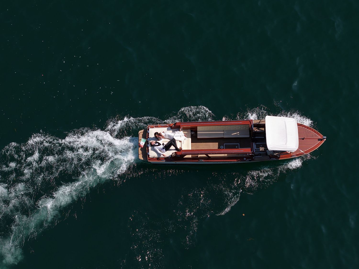 Aerial shot of classic wooden boat creating wake in dark waters.