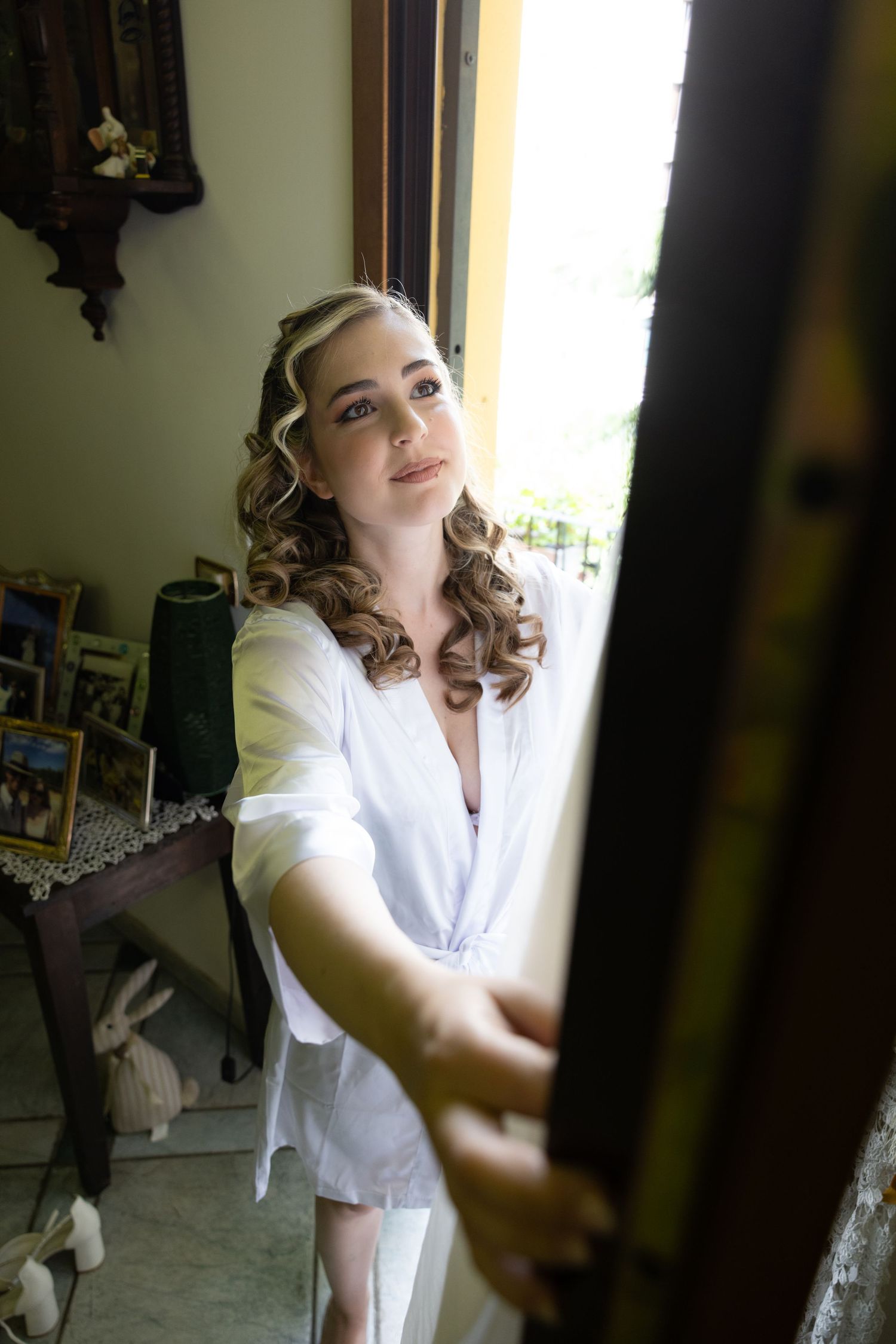 Someone in a white robe stands by a window during wedding day preparations.