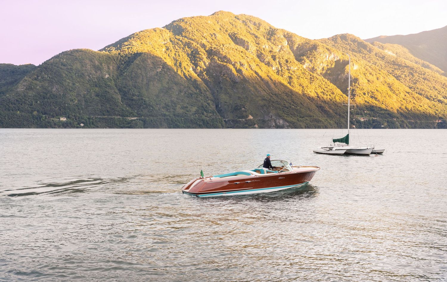 Scenic mountain lake view at sunset with boats on calm waters.