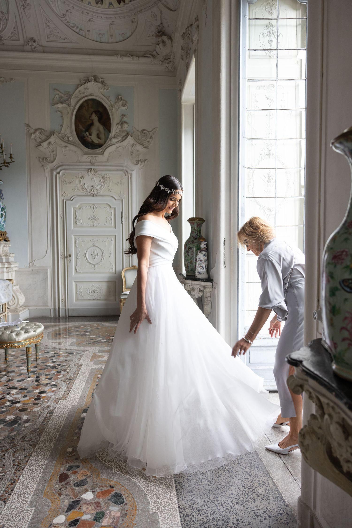 Wedding dress preparations in an ornate white room with patterned floor tiles.