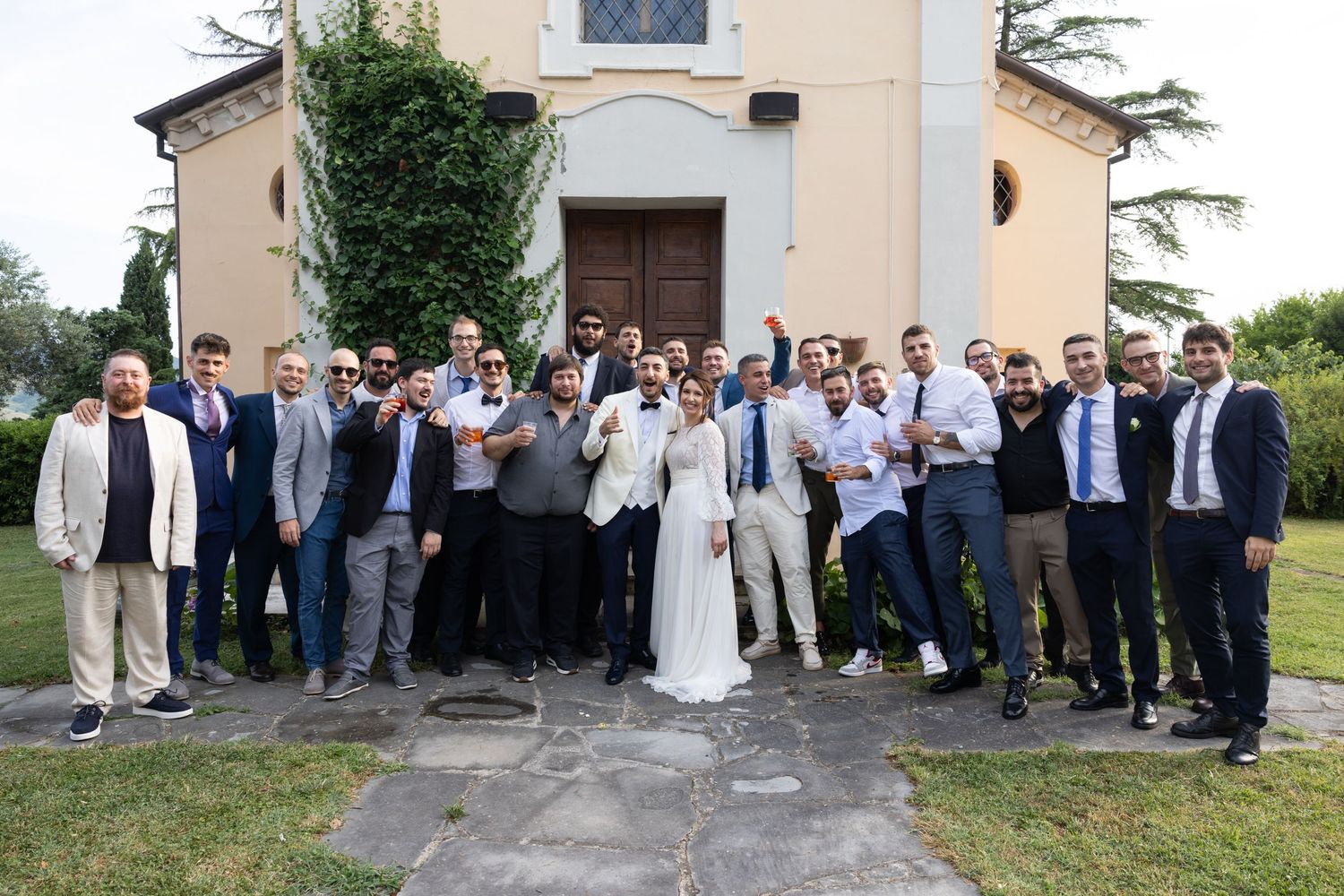 Large wedding party group photo outside church with newlyweds in center.