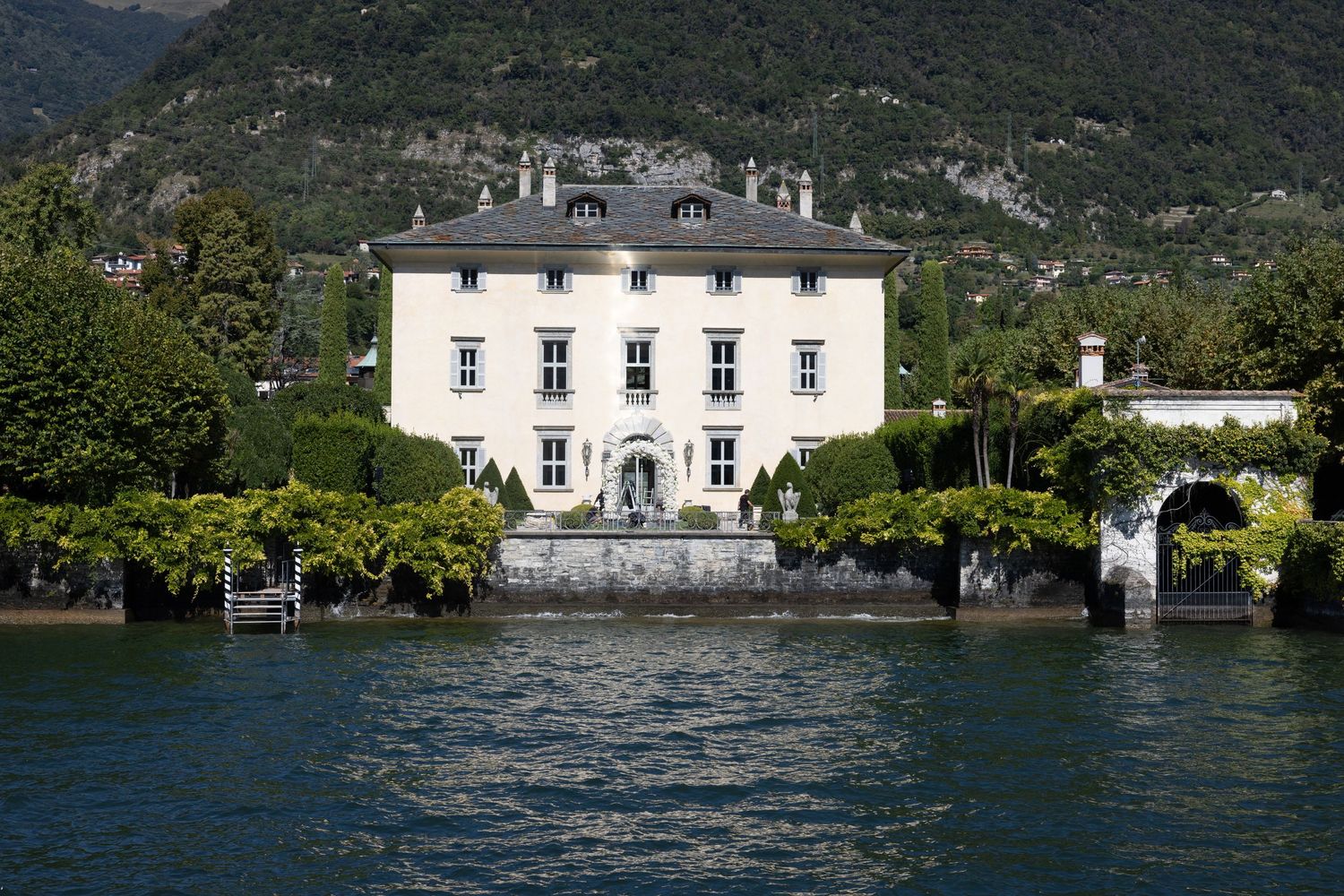 Panoramic view of a white lakeside villa with mountains in the background.