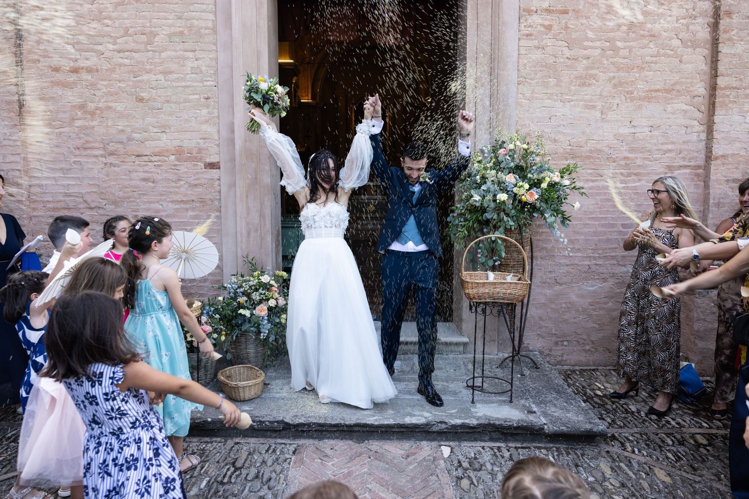Wedding guests celebrate outside a historic brick building entrance.