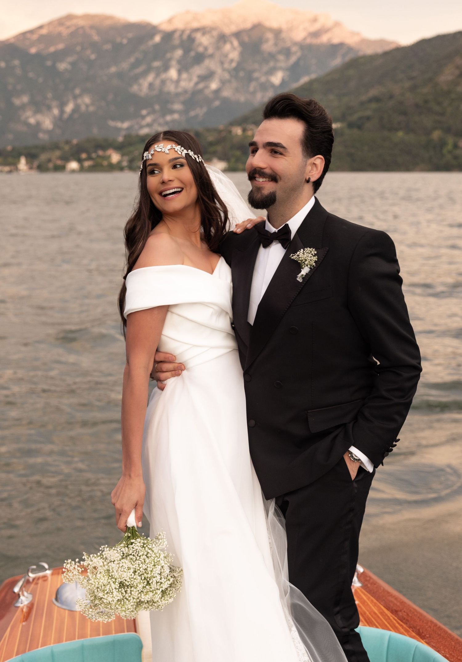 A couple enjoys their wedding day on a boat with mountains and sunset in the background.