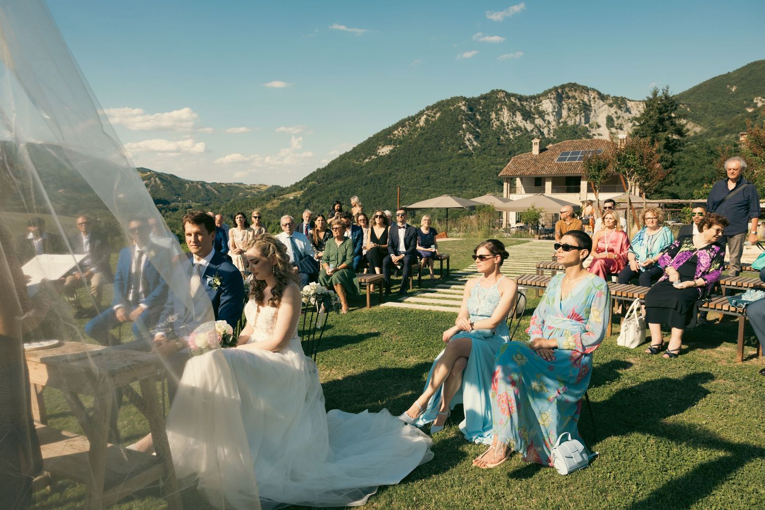 Wedding guests seated on a lawn with mountain views during an outdoor ceremony.