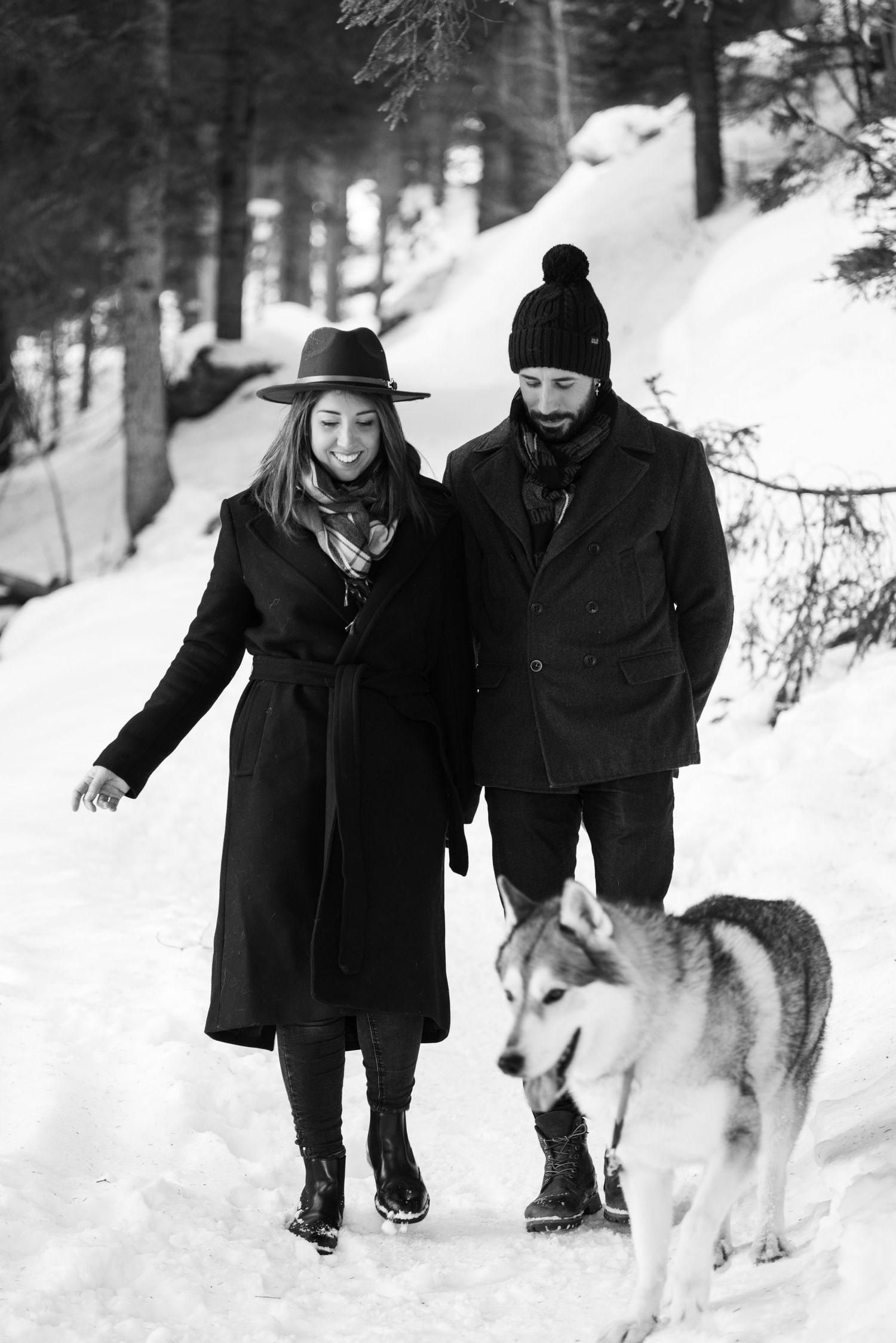 People enjoying a winter walk with their dog through a snowy forest landscape.
