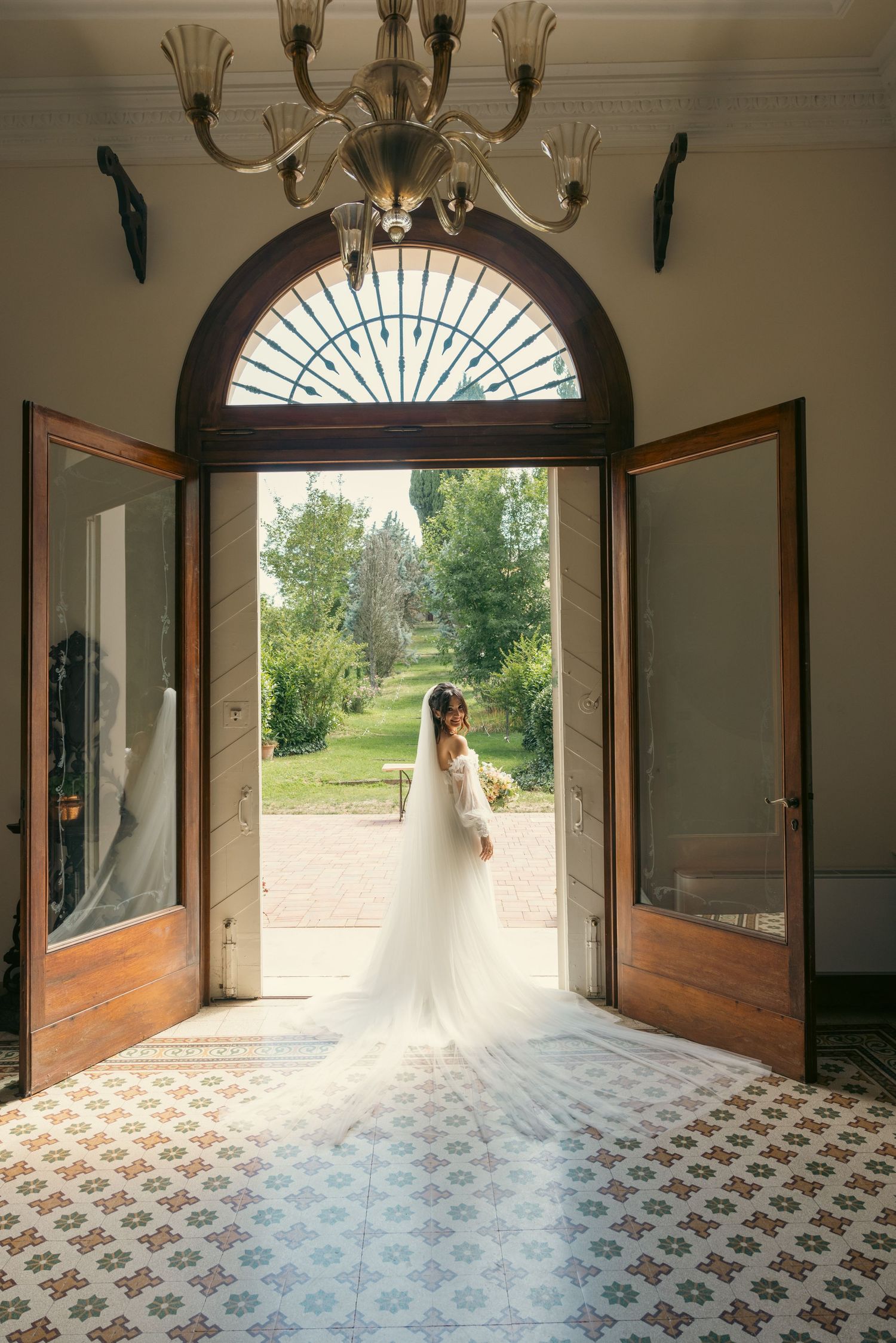 A white wedding dress silhouetted against an arched doorway with natural light streaming in.